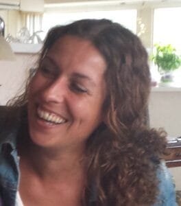 Oesiana lacht, met donkere krullen, binnen bij het raam