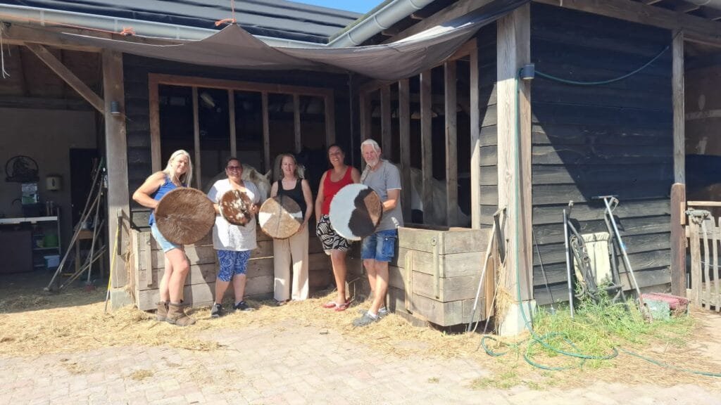 Vijf deelnemers houden hun zelfgemaakte sjamanendrums vast bij een stal
