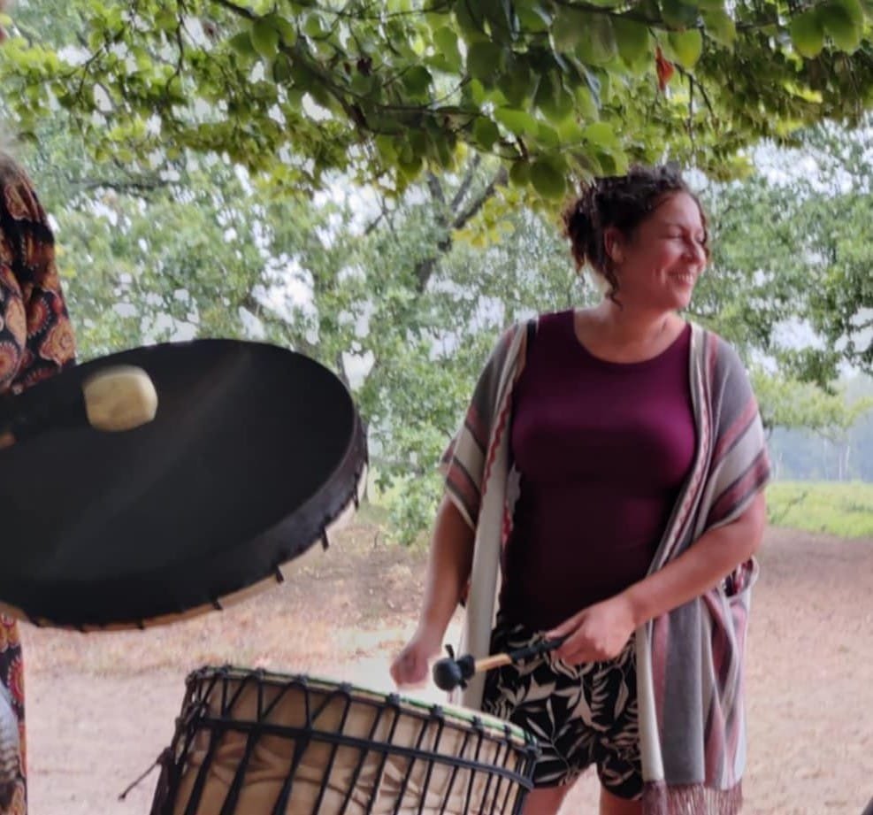 Oesiana speelt djembe buiten onder de bomen tijdens een drumsessie