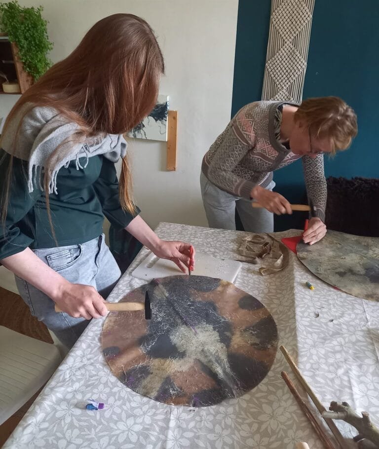 Twee deelnemers slaan met hamer en pons gaten in de rand van een drumhuid