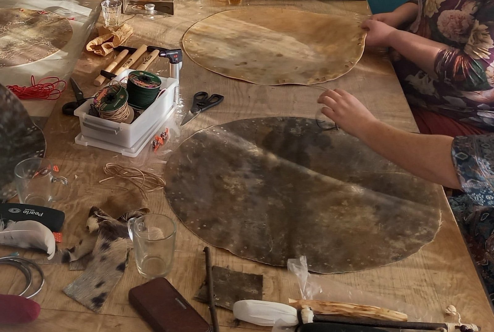 Twee ronde huiden op een houten werktafel met spoelen touw, een schaar en gereedschap ertussen