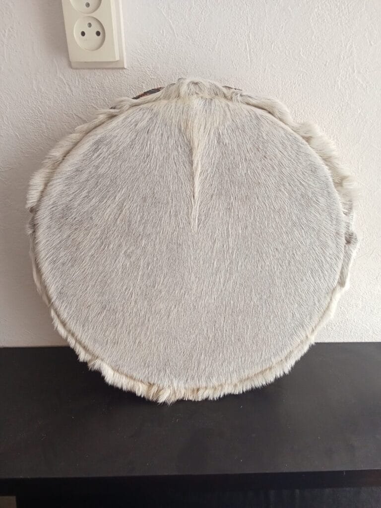 Een sjamanendrum met lichte langharige huid hangt aan een witte muur
