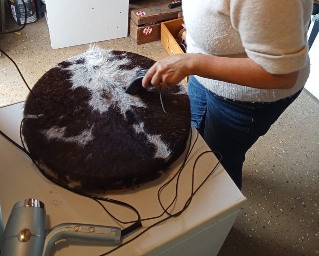 Een sjamanendrum wordt met warme lucht gedroogd op een werkbank, met een föhn op de voorgrond