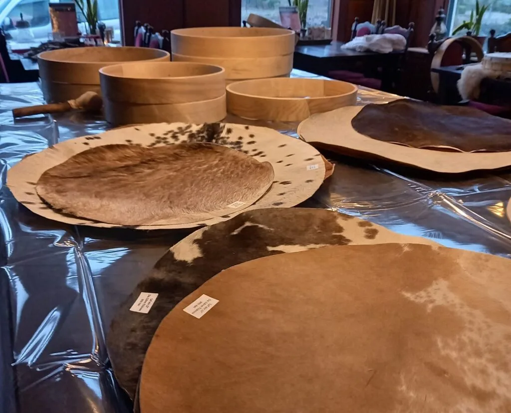 Essenhouten drumframes in verschillende maten naast gevlekte huiden op tafel