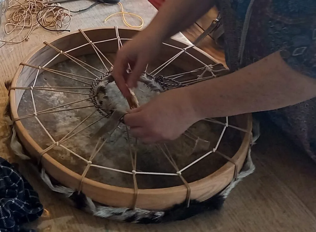 Twee handen spannen het touw van een sjamanendrum aan op een houten tafel