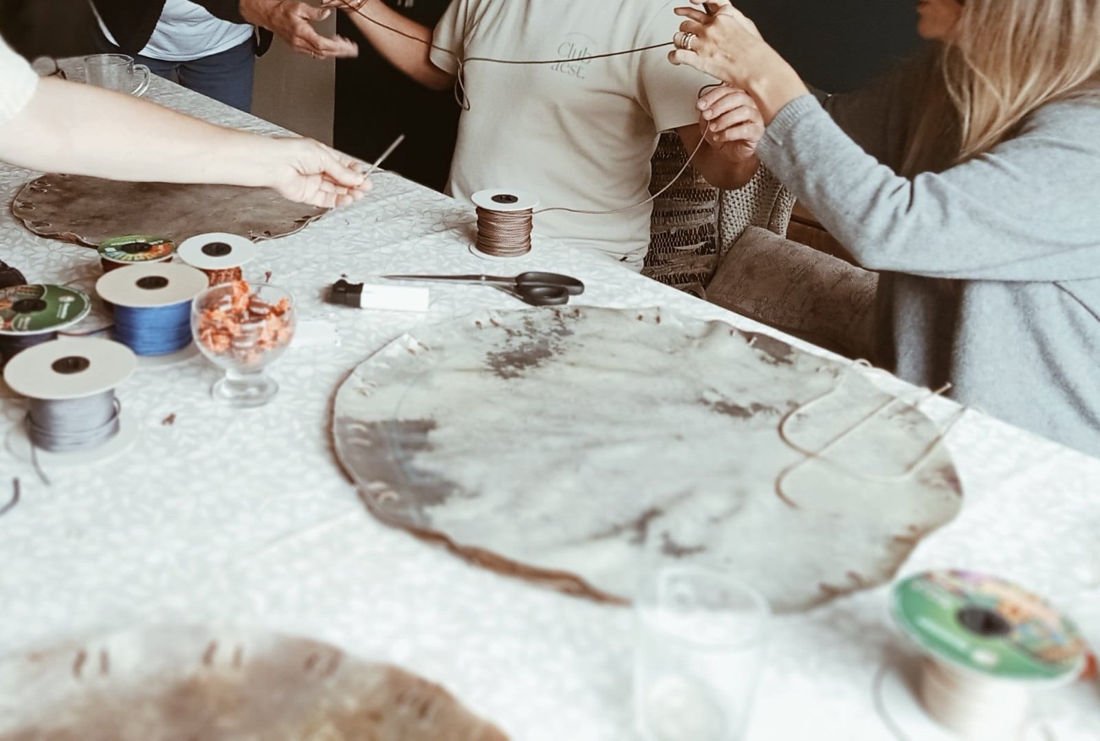 Deelnemers rijgen het touw door de gaten in de huiden, met spoelen touw en een schaar op tafel
