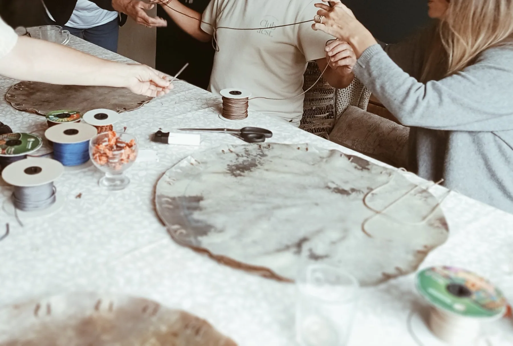 Deelnemers rijgen het touw door de gaten in de huiden, met spoelen touw en een schaar op tafel